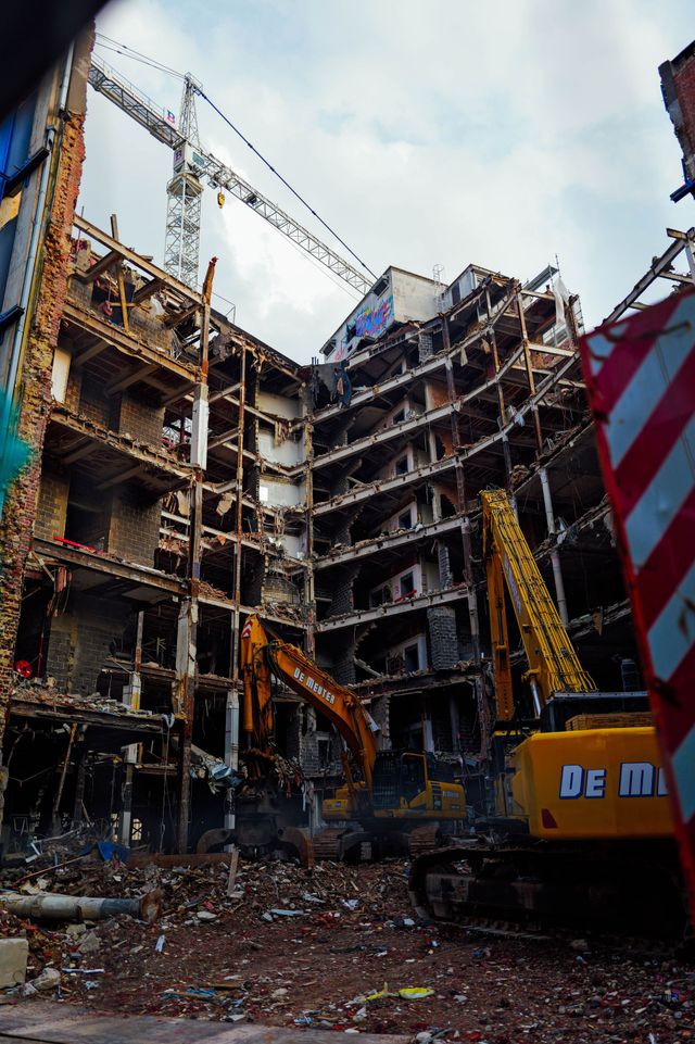Damaged multi-story building under demolition, with excavator and rubble in the foreground