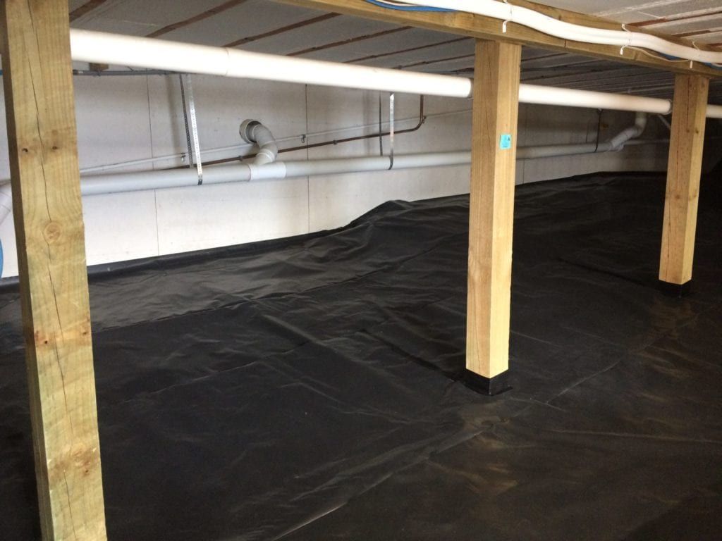 Black plastic sheeting covers a crawl space floor, wooden support beams and white pipes visible above.