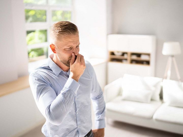Man pinching his nose, indicating a bad smell, in a bright living room.