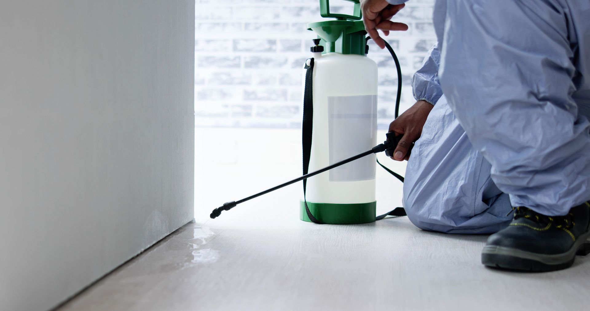 Person in protective suit spraying a white floor with a green and white pesticide tank.