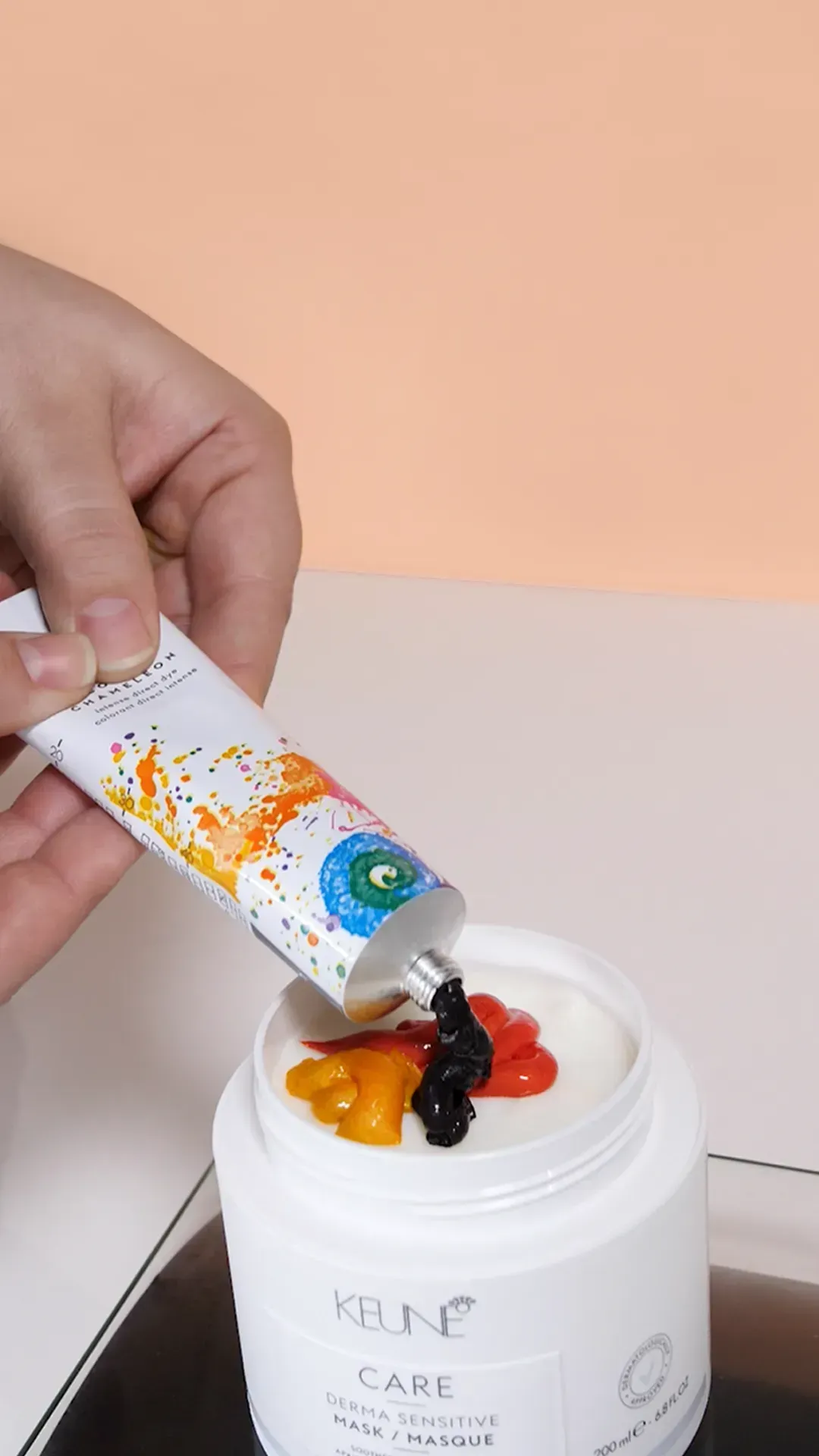Hand squeezing colorful tube onto a white cream jar with orange and black pigment accents