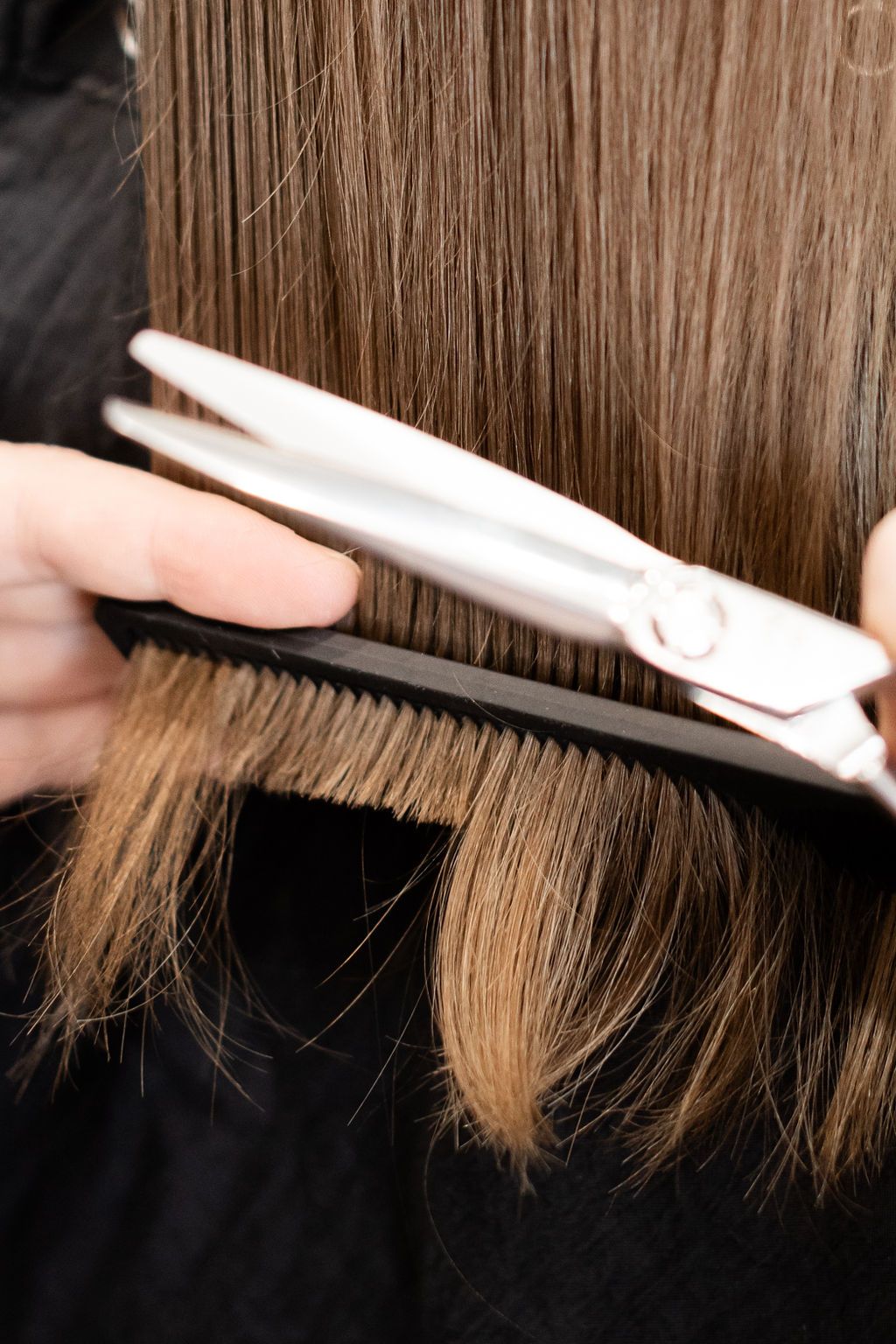 Stylist curling a client’s hair in a salon, with an intricate half-up style visible from the back