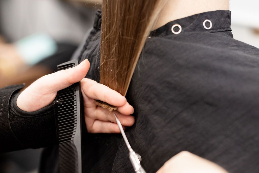 Stylist braiding a person’s dark hair in a salon, creating a twisted updo hairstyle