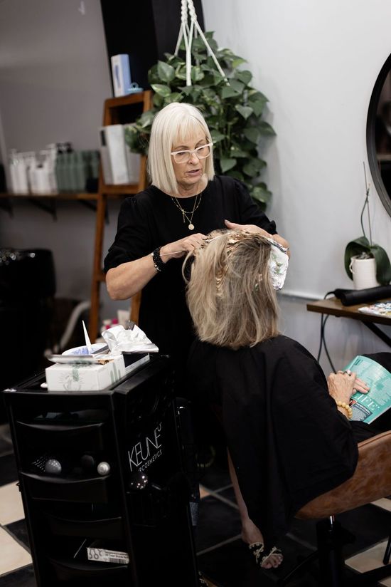 Stylist cutting a client’s long hair in a salon chair beside a mirror