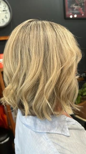Blonde wavy bob haircut with soft highlights, shown from the back in a salon.