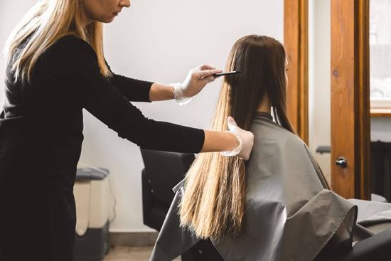 Stylist cutting a client’s long hair in a salon chair beside a mirror