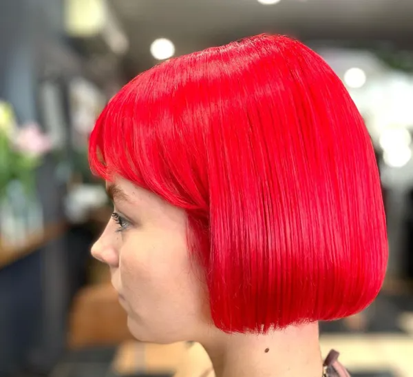 Side-profile portrait with a bright red bob haircut against a blurred indoor background