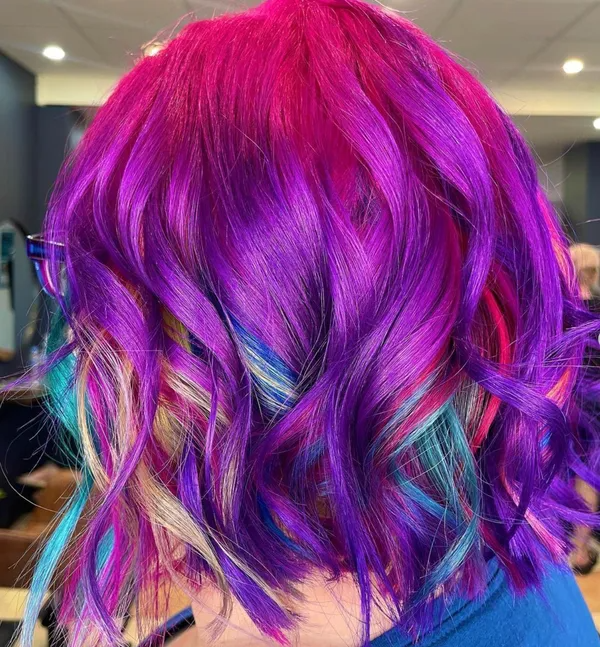 Close-up of wavy magenta and purple hair with teal highlights, viewed from behind.