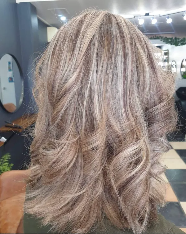 Blonde layered shoulder-length hair with soft curls, shown from the back in a salon.