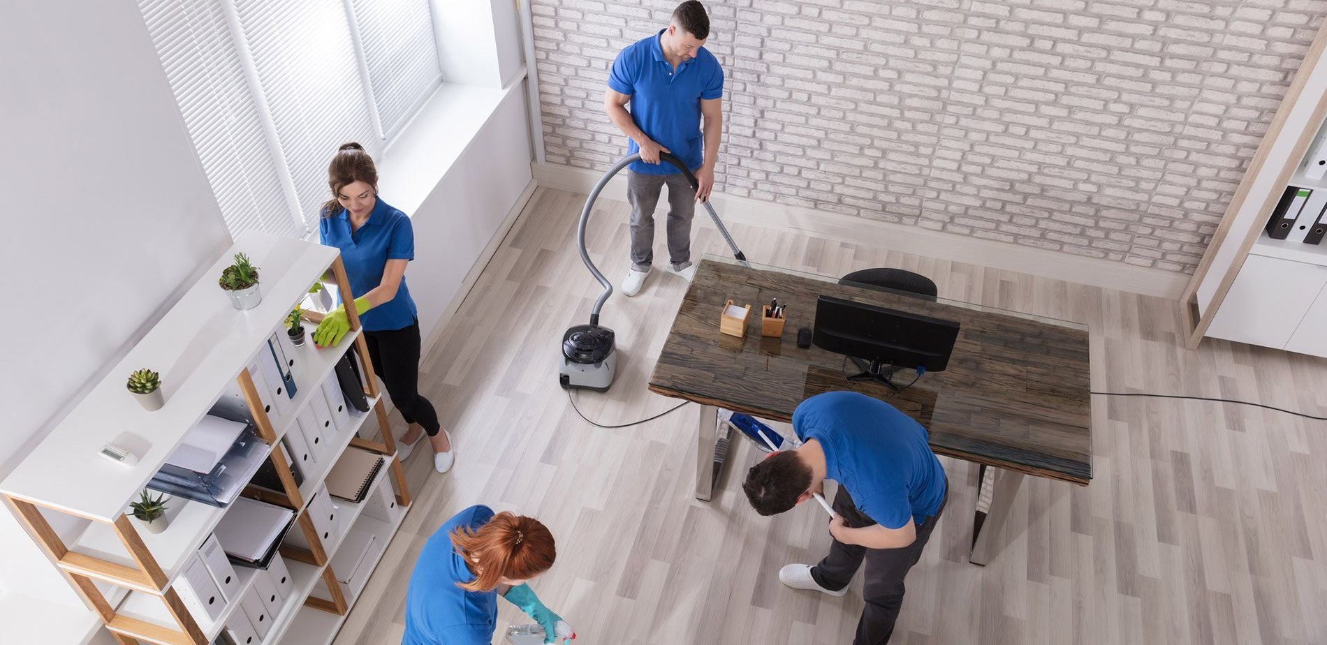 People cleaning a bright room with mops, a vacuum, and a table