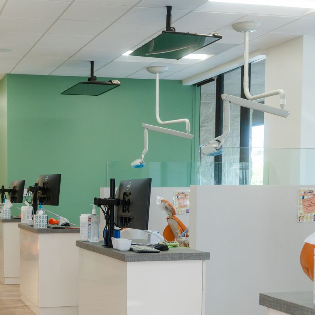 Modern dental clinic reception with white counters, mint green wall, and treatment chairs behind glass partitions