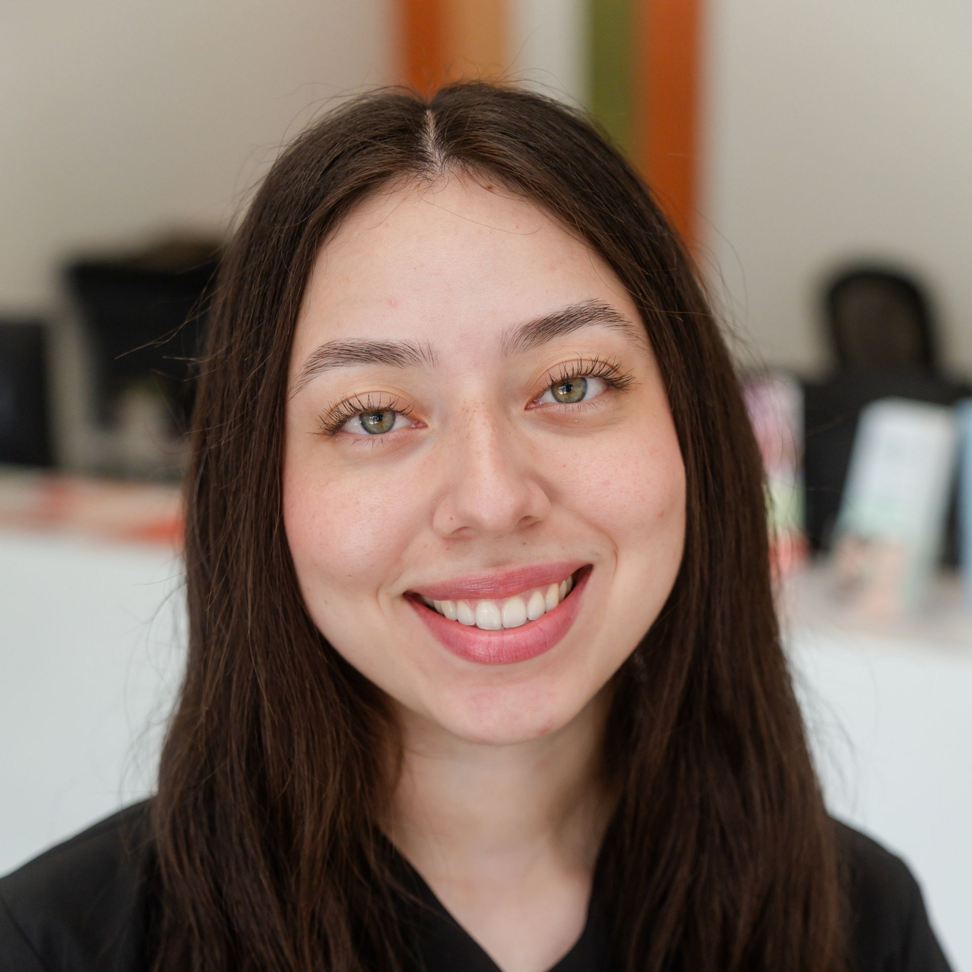 Smiling person with long brown hair in a bright office setting