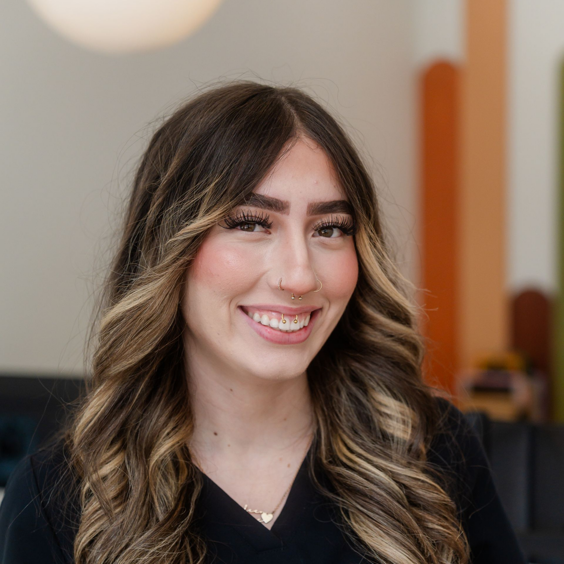 Smiling woman with long wavy hair in a black top, indoors against a blurred background.