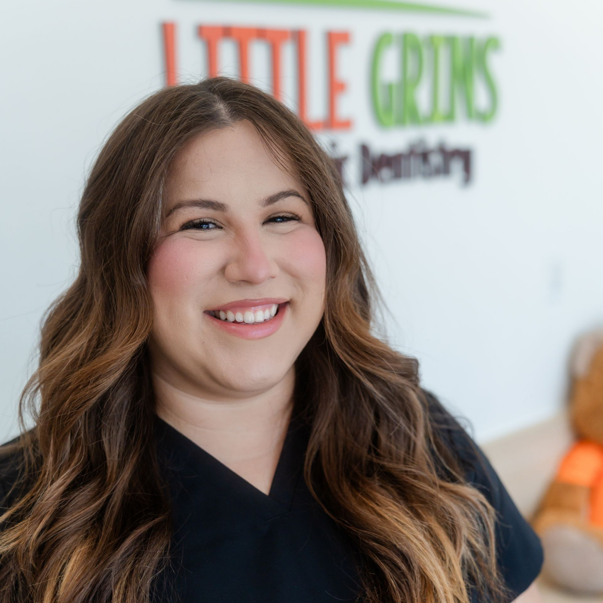 Smiling woman in a black top standing in front of a Little Girls Dentistry sign