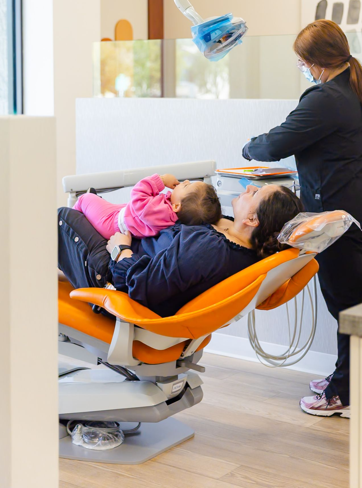 Dental exam with patient in orange chair and clinician working in a bright clinic