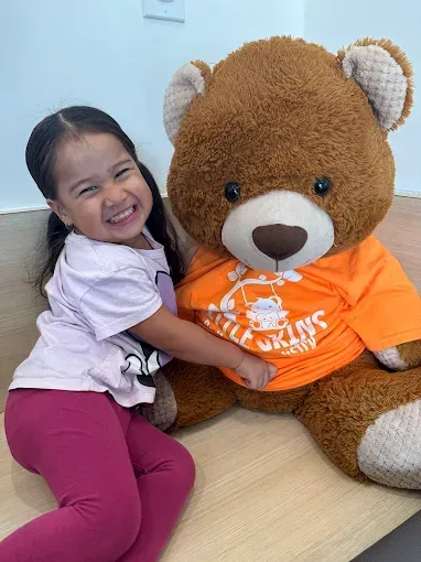 Child hugging a large teddy bear wearing an orange shirt on a couch, both smiling.