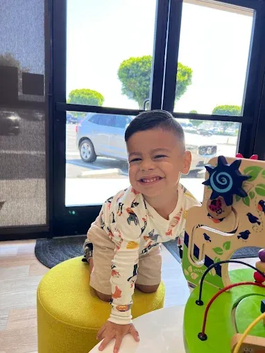 Smiling child on a yellow cushion playing with a toy in front of a bright window