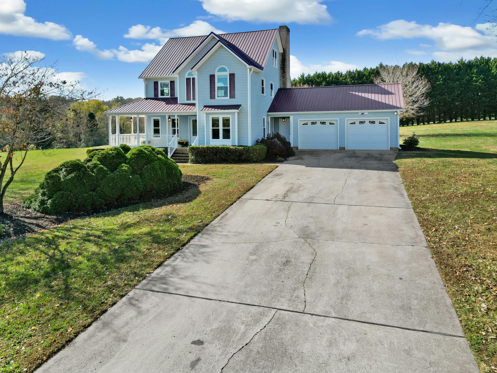 Two-story blue house with white garage, front porch, and long driveway on a sunny day