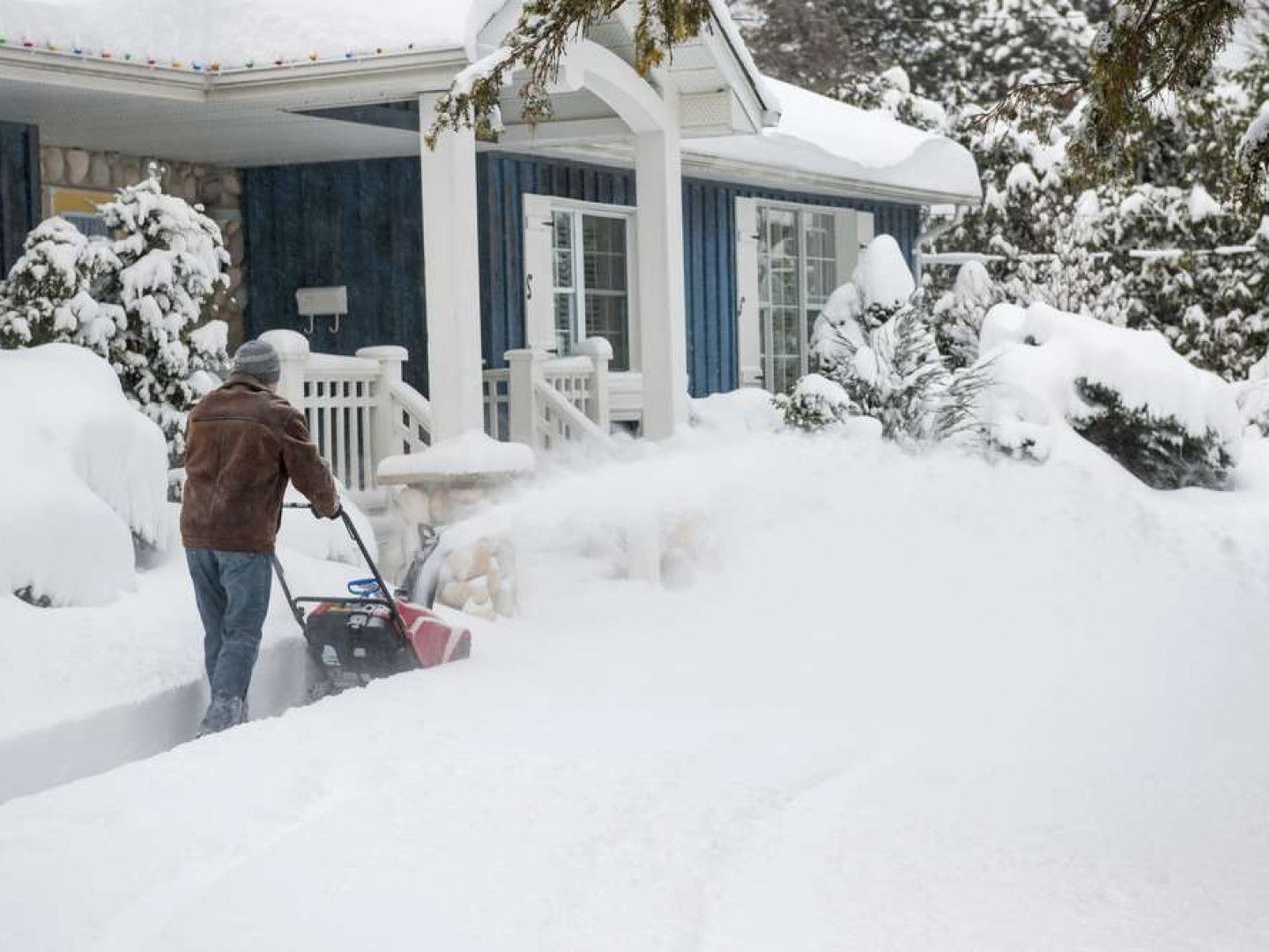 Person clearing deep snow from a blue house walkway with a snow blower