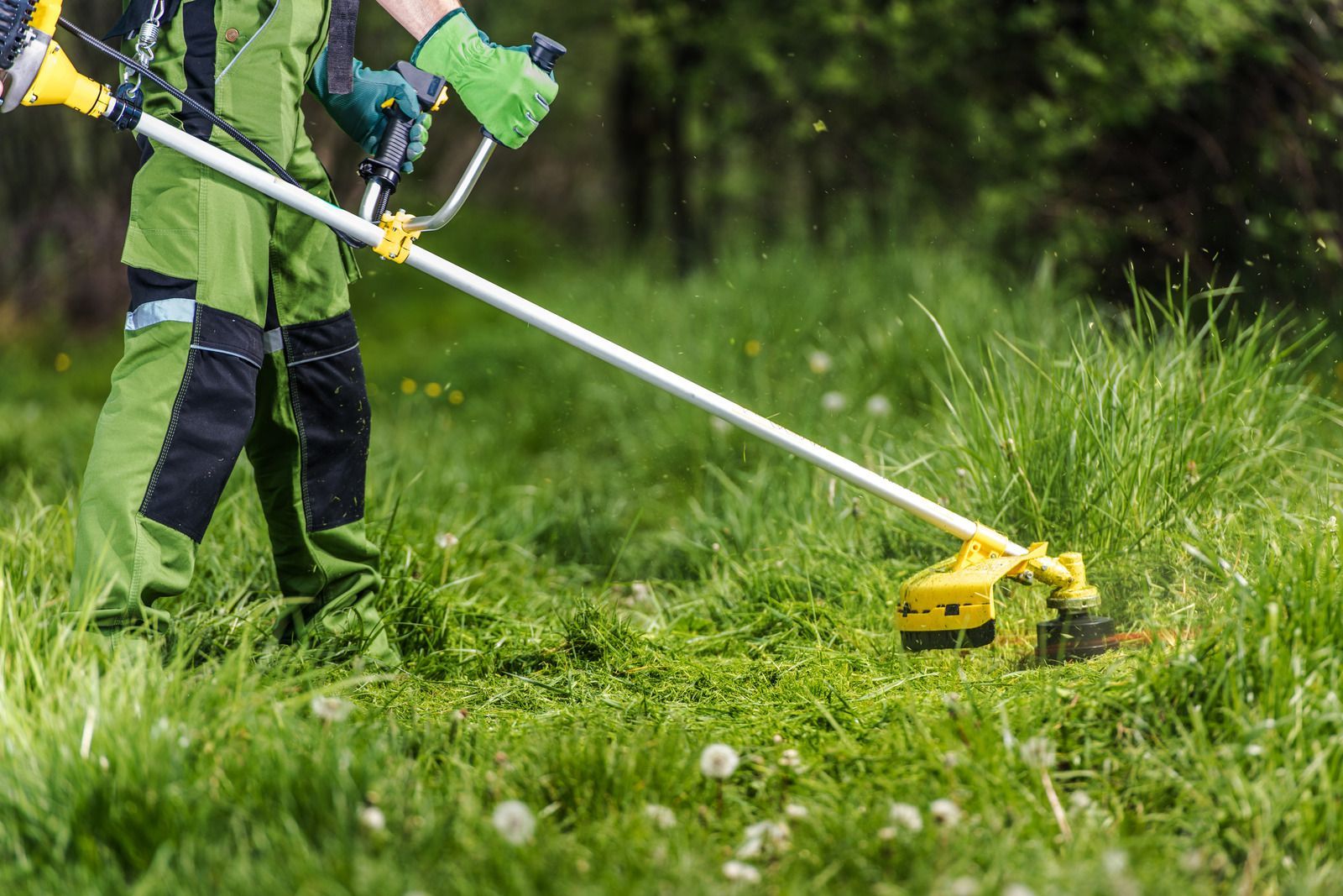 Person using a yellow string trimmer in tall grass outdoors