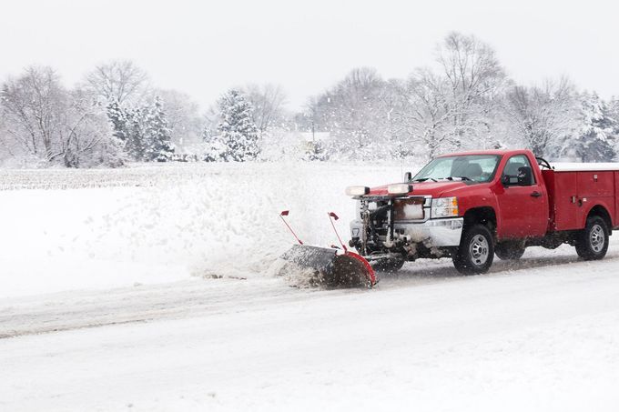 Red pickup truck plowing snow on a snowy roadside with trees in the background