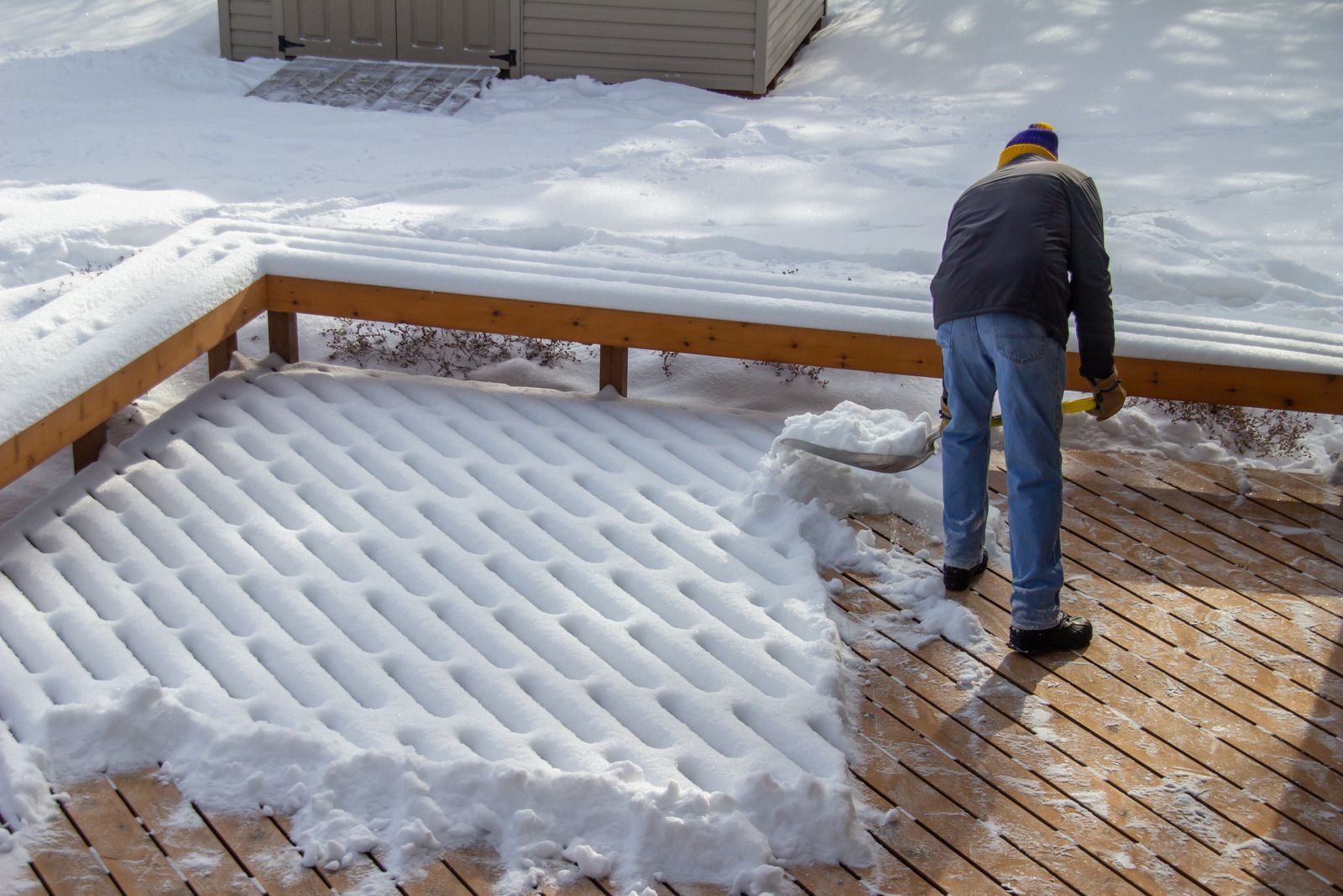 Person shoveling snow from a wooden deck in winter