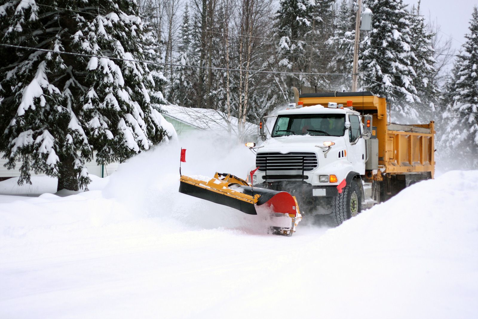 Snowplow truck clearing a snowy road in a forested area
