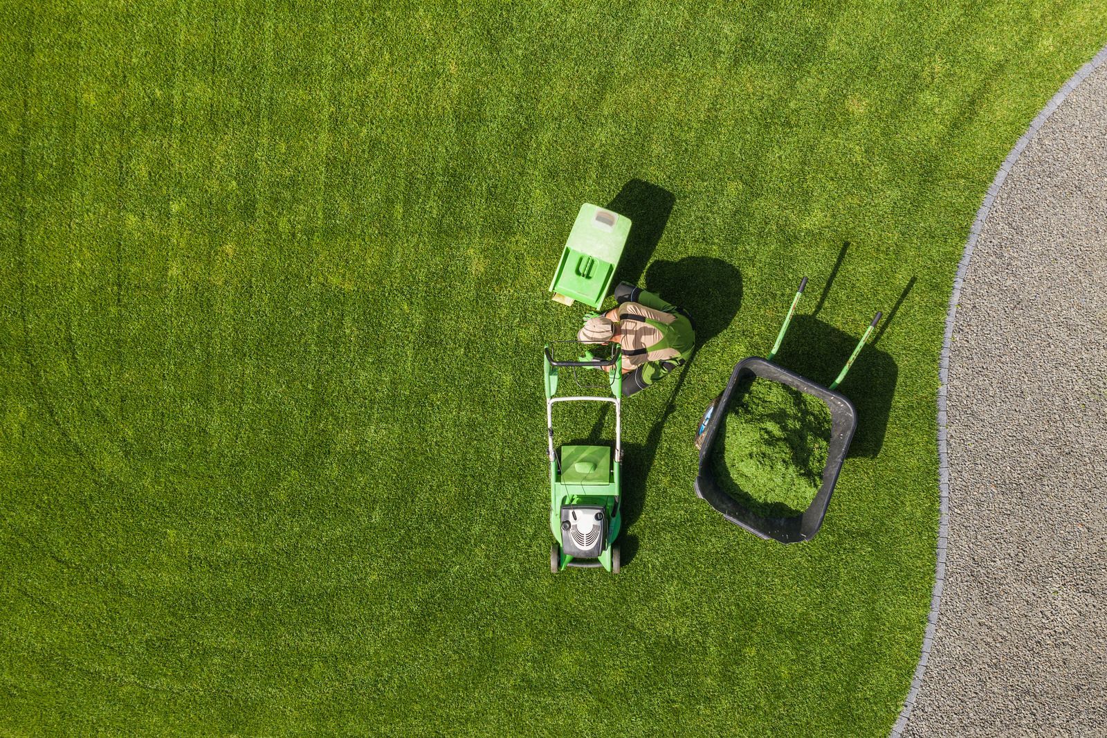 Person mowing a bright green lawn with a push mower beside a gravel path