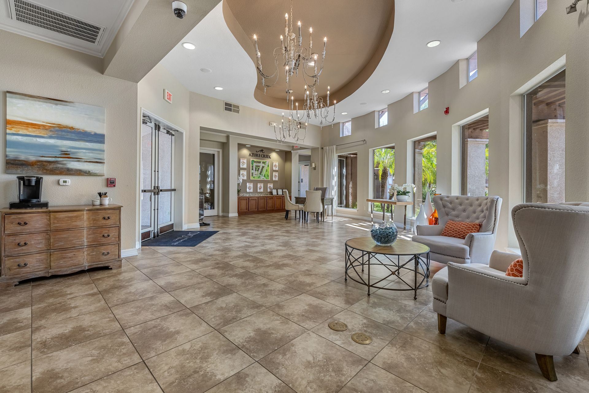 Bright lobby with tiled floor, chandelier, artwork, and seating near large windows