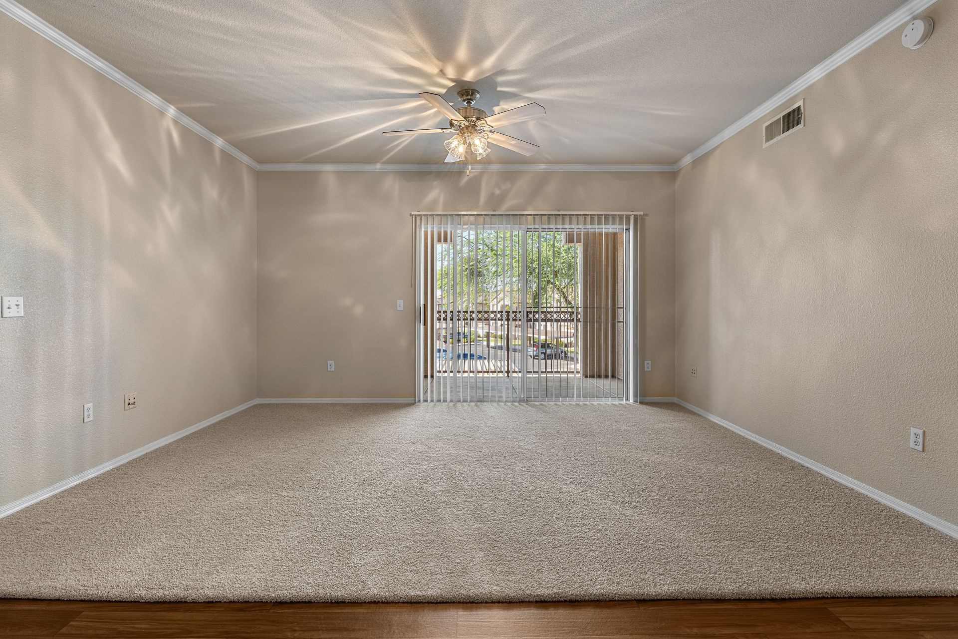 Empty beige living room with carpet, ceiling fan, and sliding glass doors to a balcony