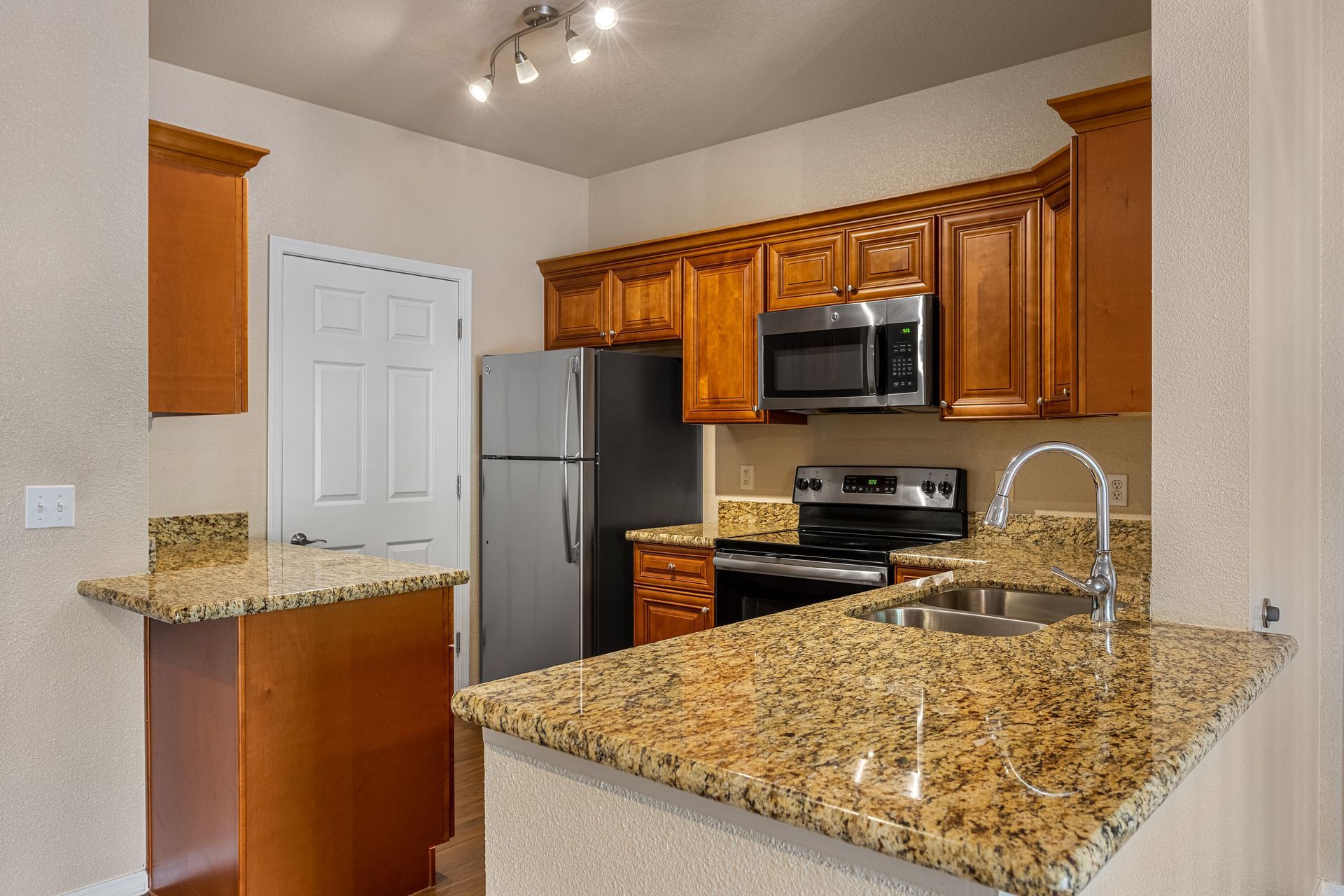 Modern kitchen with granite countertops, wood cabinets, stainless appliances, and a white pantry door