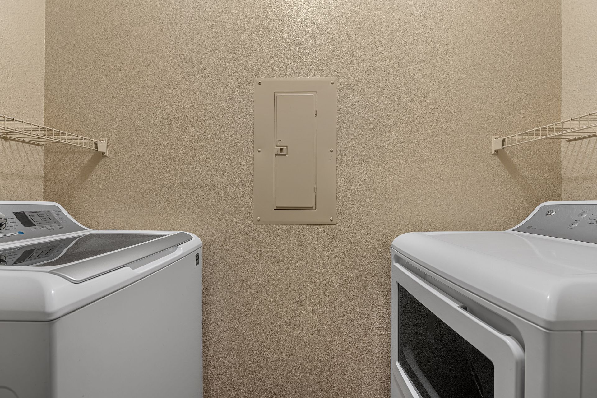 Laundry room with two white washers facing a beige wall and utility panel.