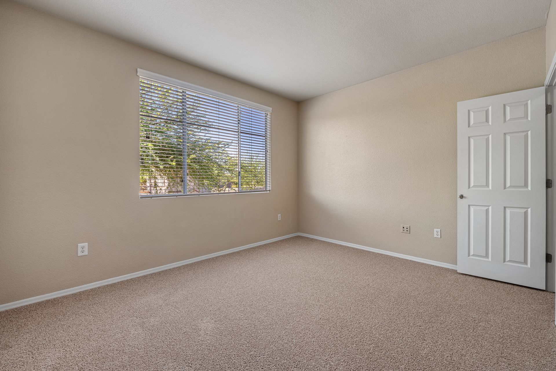 Empty beige bedroom with carpet, window, and open white closet door