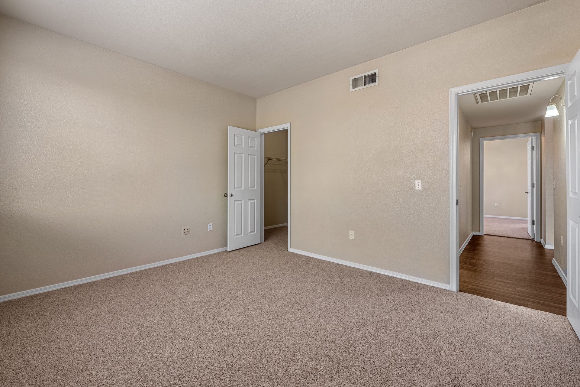 Empty beige bedroom with carpet, open door, and hallway visible through a doorway