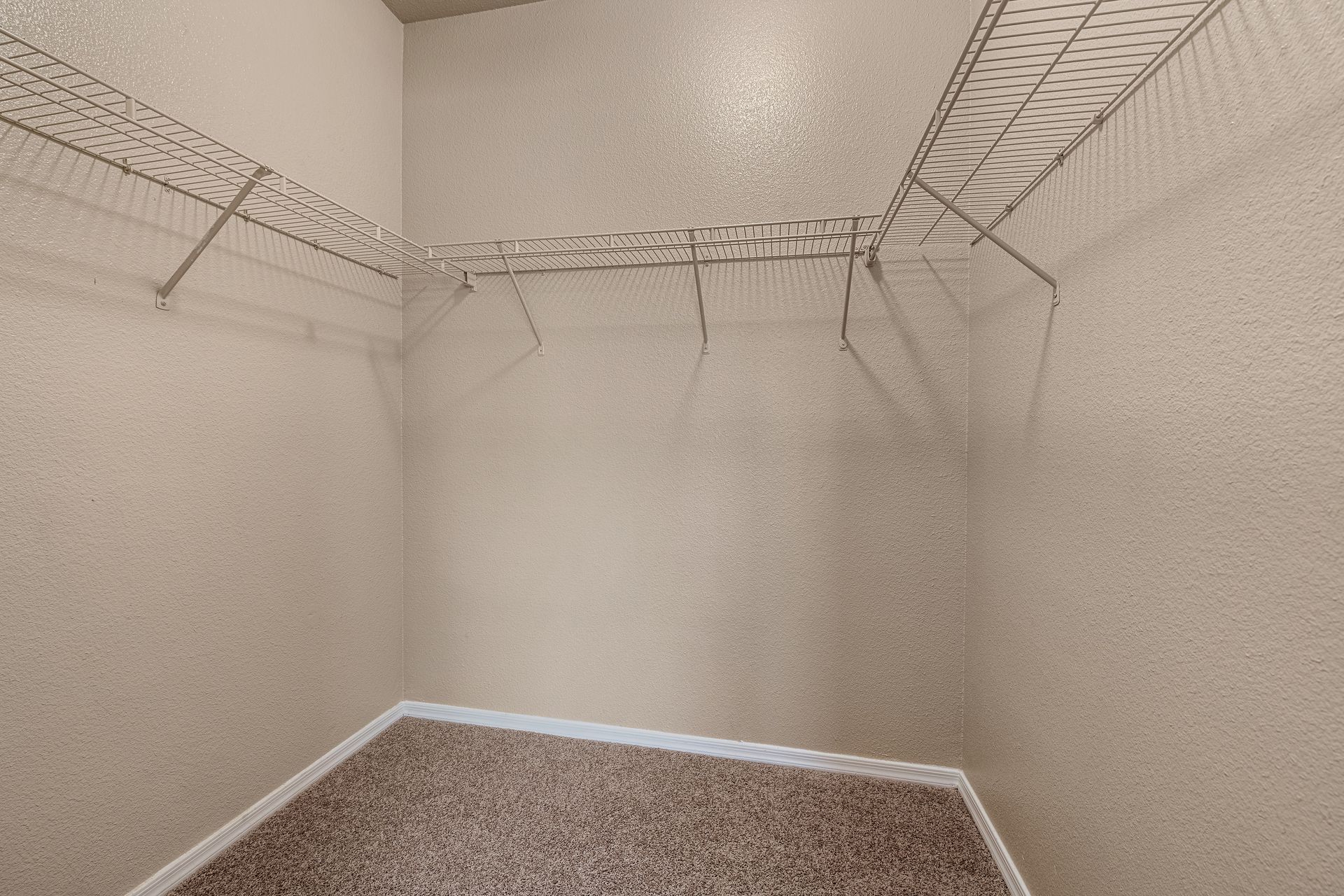 Empty beige walk-in closet with wire shelving and carpeted floor