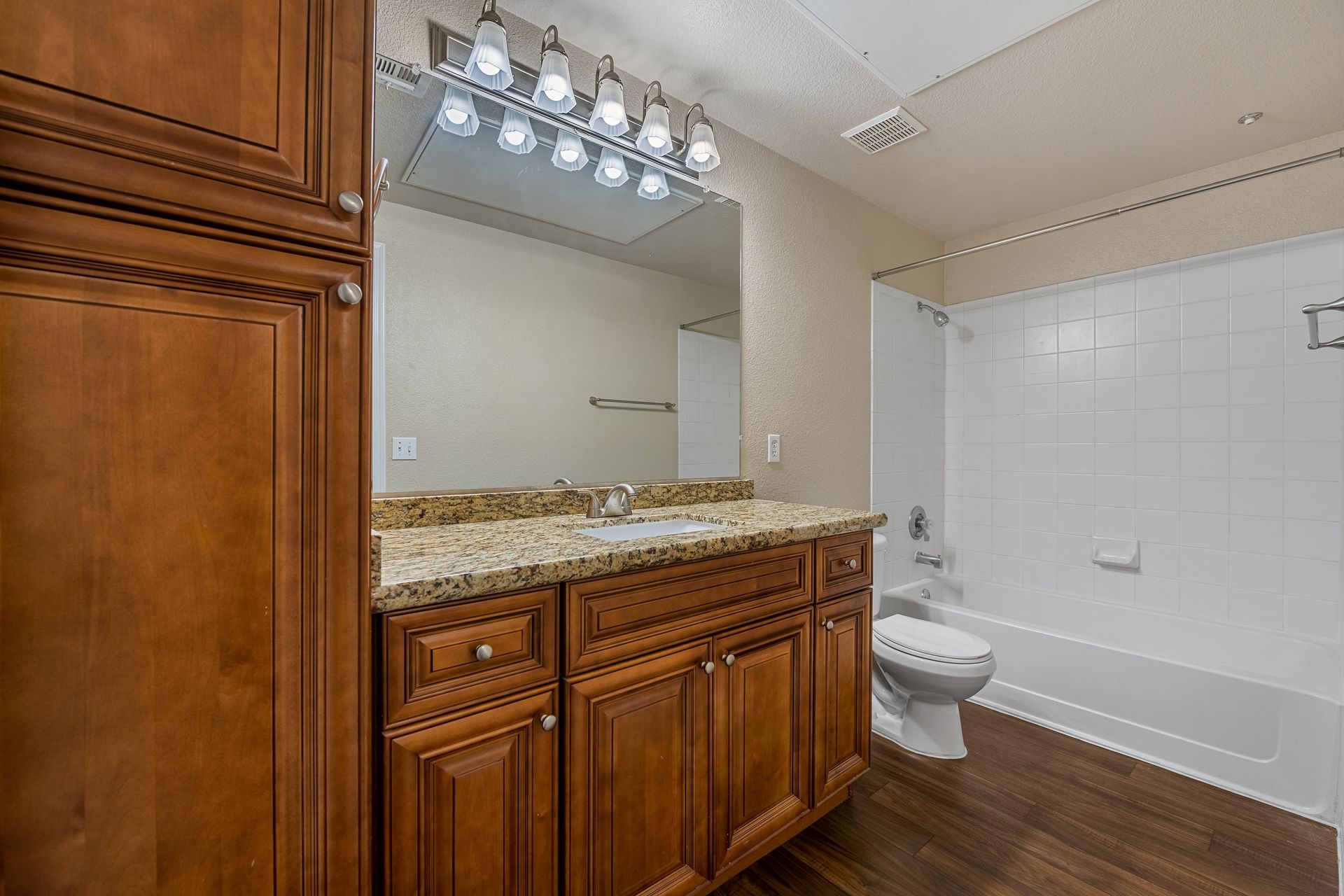 Bathroom vanity with granite countertop, large mirror, and adjacent bathtub with white tile surround.