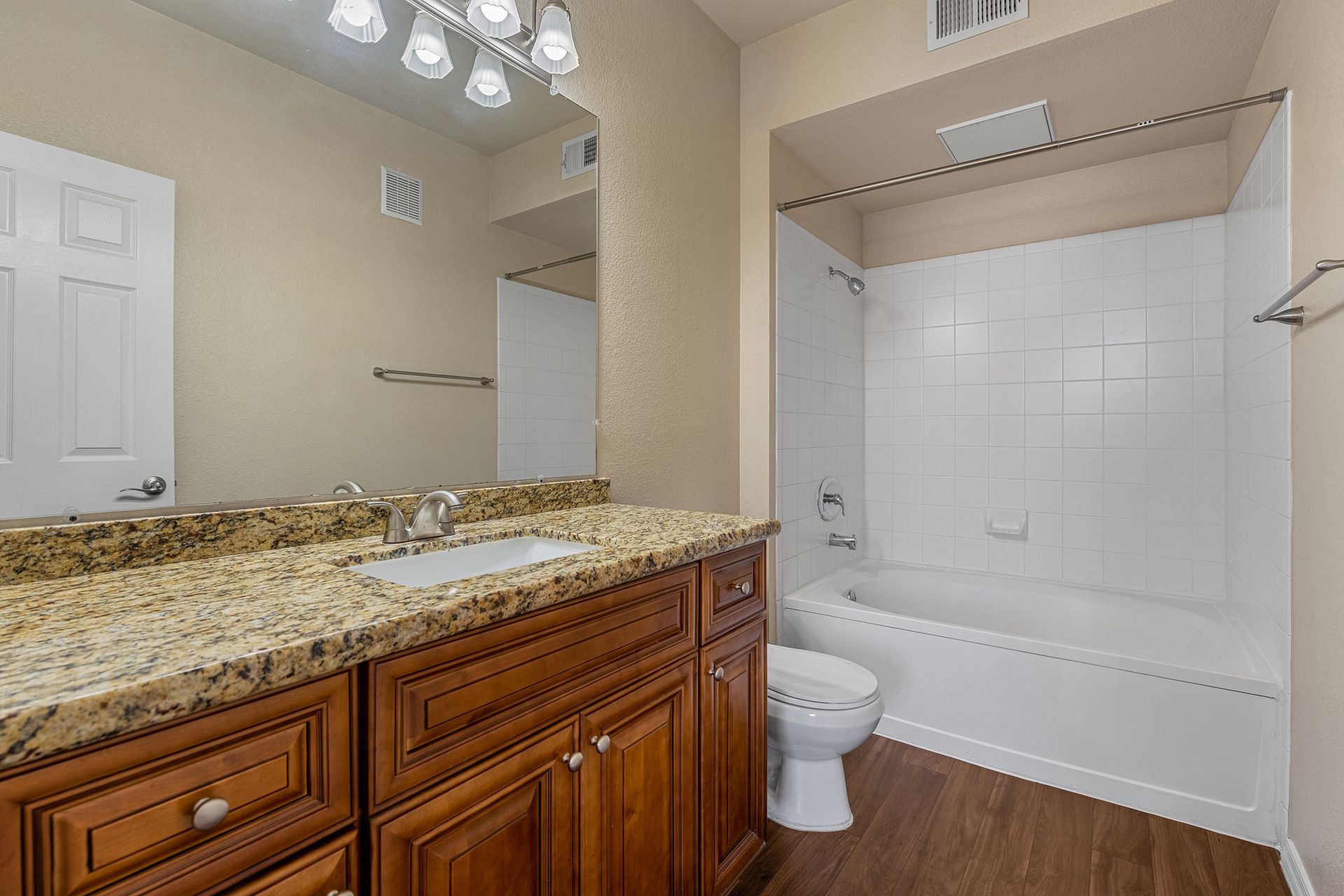 Bathroom with granite vanity, large mirror, toilet, and white shower/tub combo.