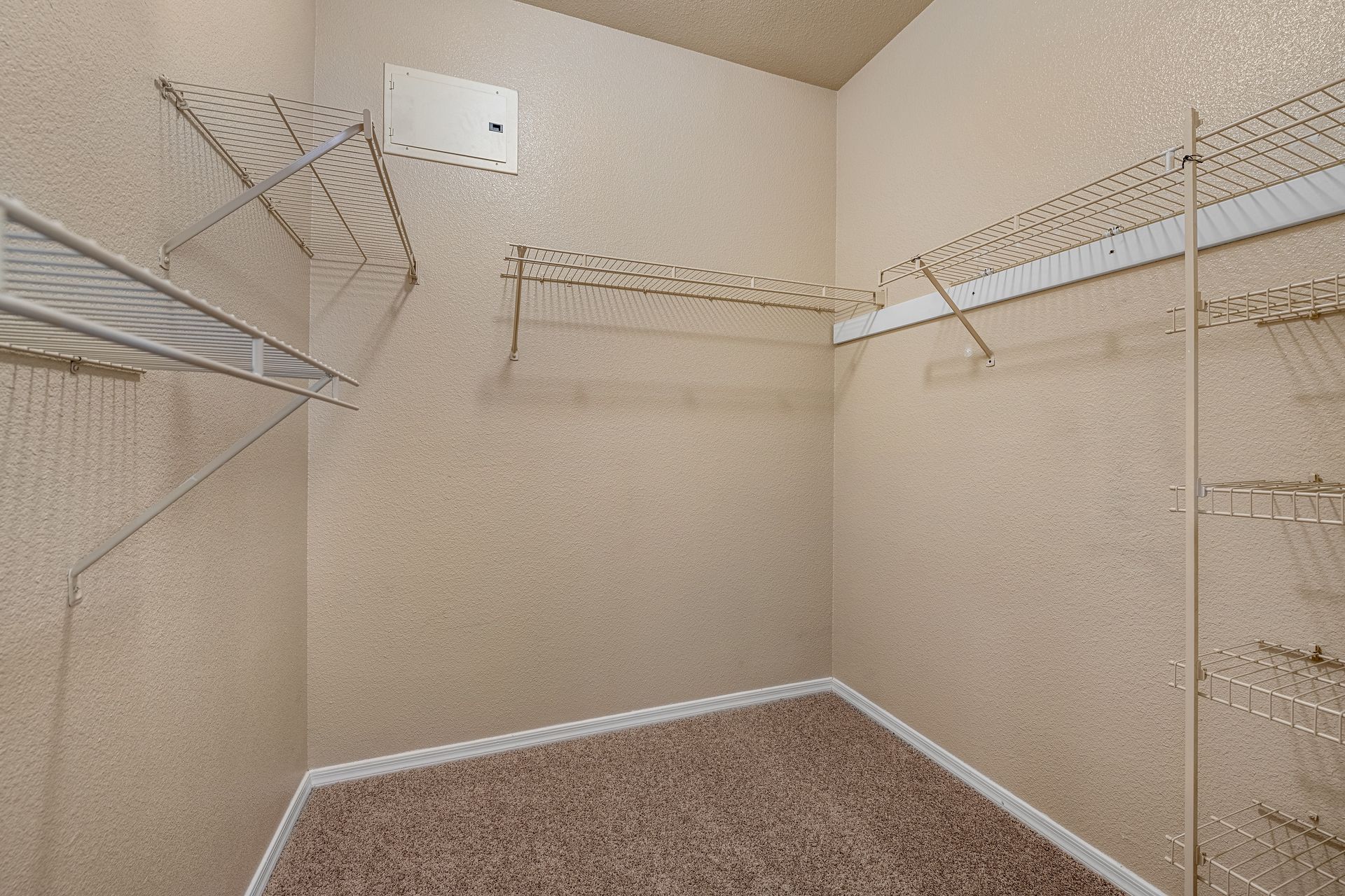 Empty beige walk-in closet with white wire shelving and carpeted floor.