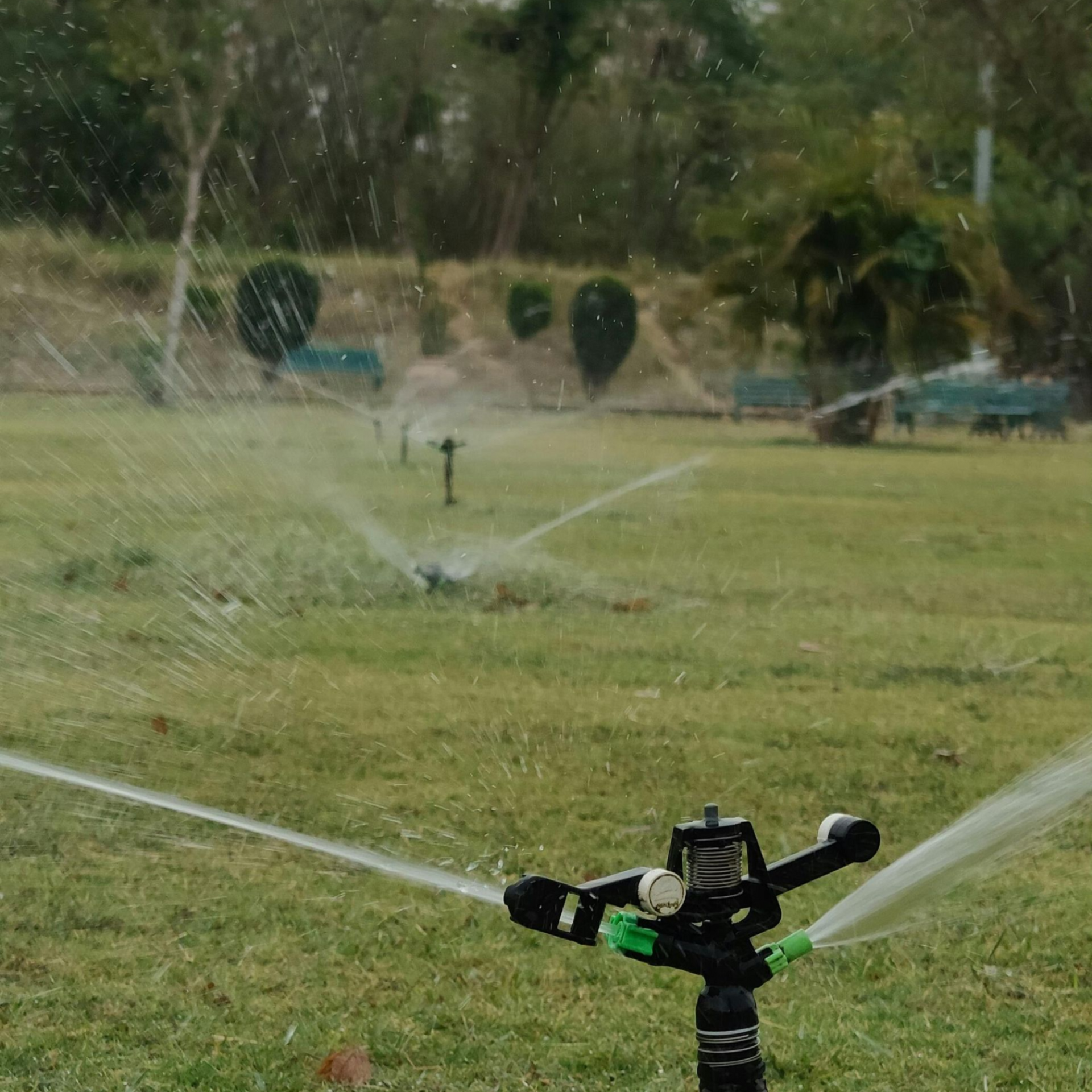 An impact sprinkler sprays water over a green grass field, with additional sprinklers visible in the background.