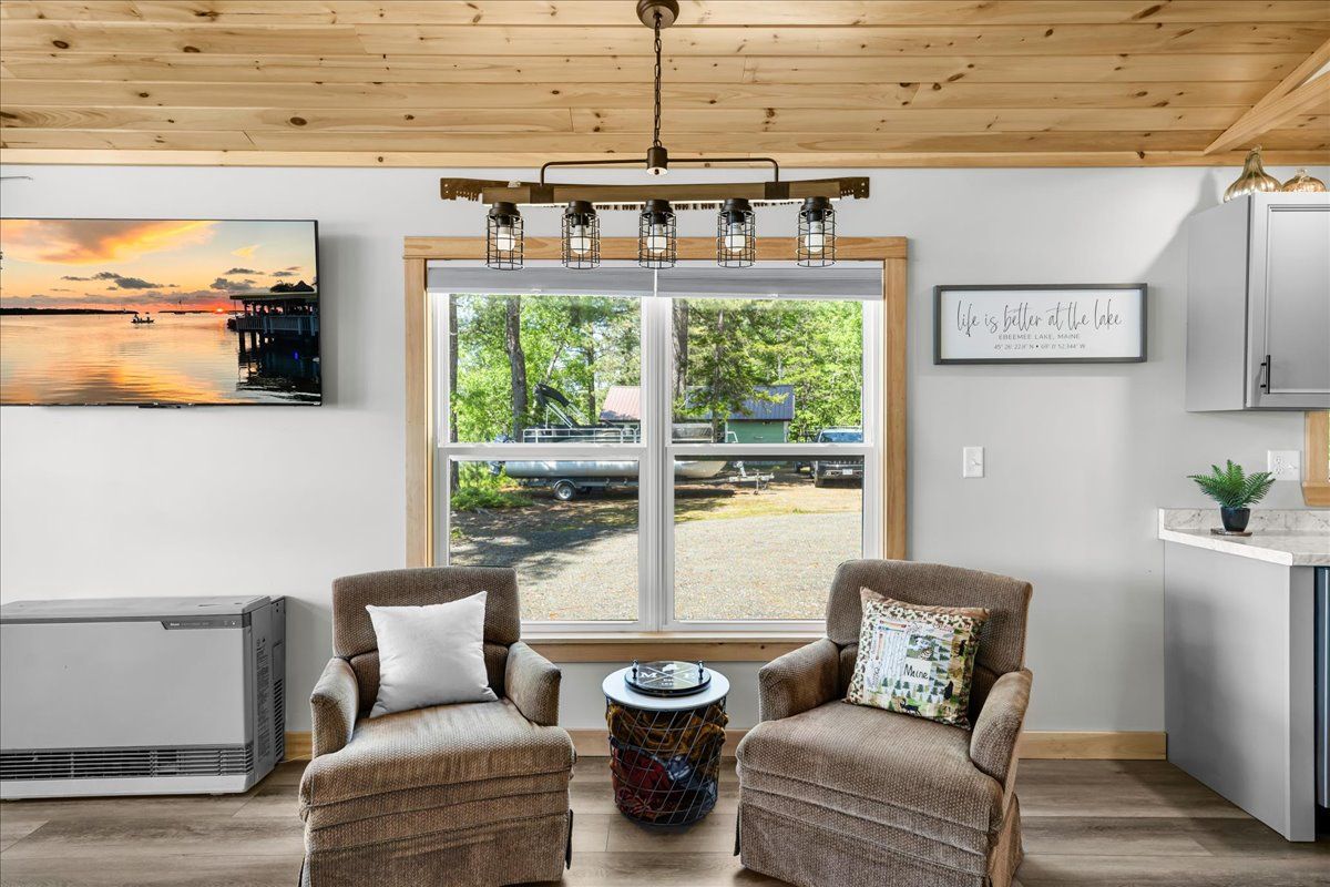 Cozy living room with two wicker chairs, a window view, wall art, and a wood plank ceiling