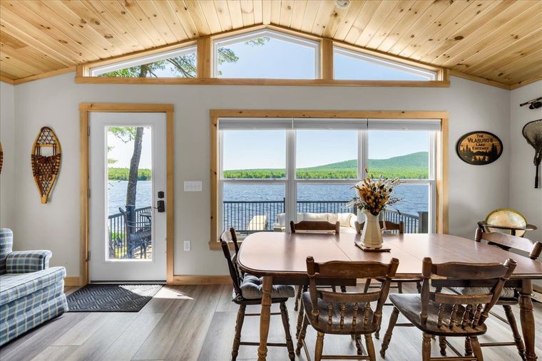 Bright dining room with wood ceiling, large windows, and a lake view beyond a wooden table and chairs