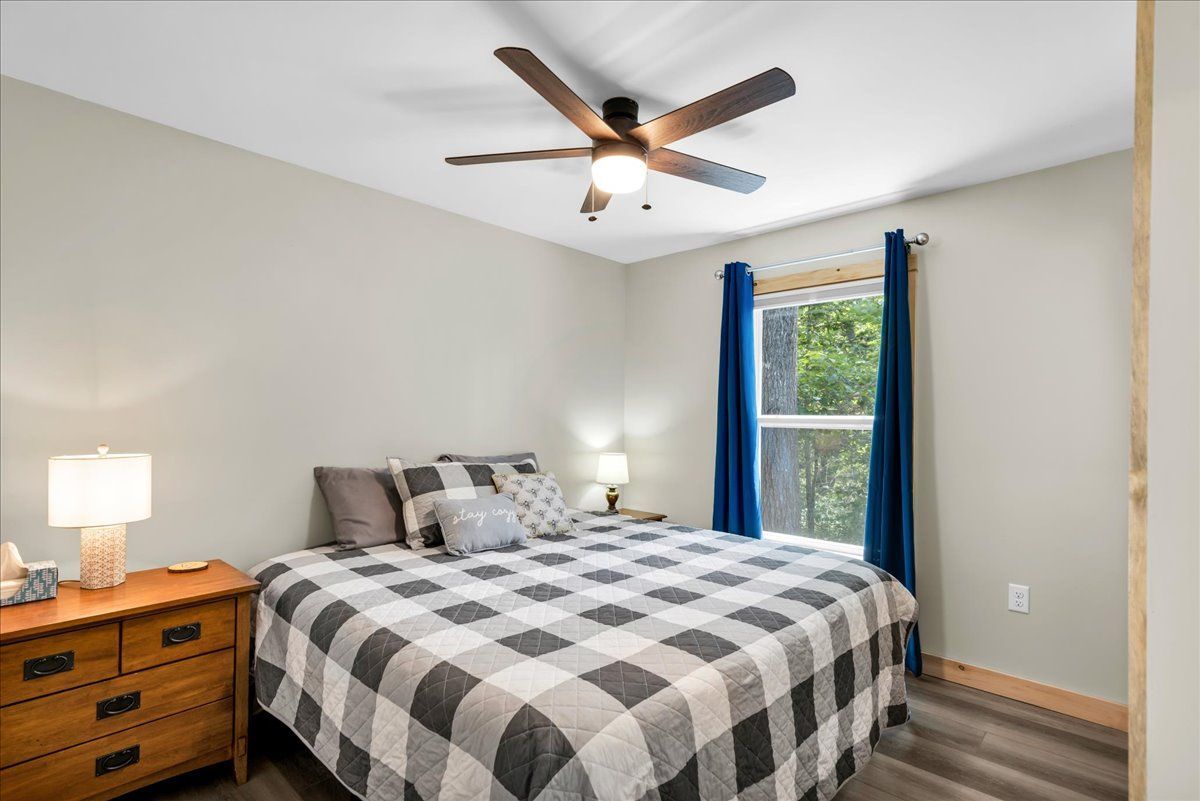 Cozy bedroom with a plaid bedspread, wooden nightstands, ceiling fan, and window with blue curtains