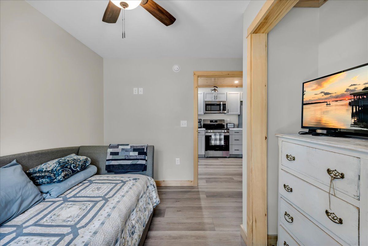 Small bedroom with gray walls, daybed, and dresser, looking into a kitchen area in the background