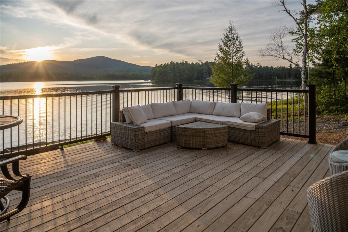 Sunset view from a wooden deck with wicker patio sofa overlooking calm water and distant mountains