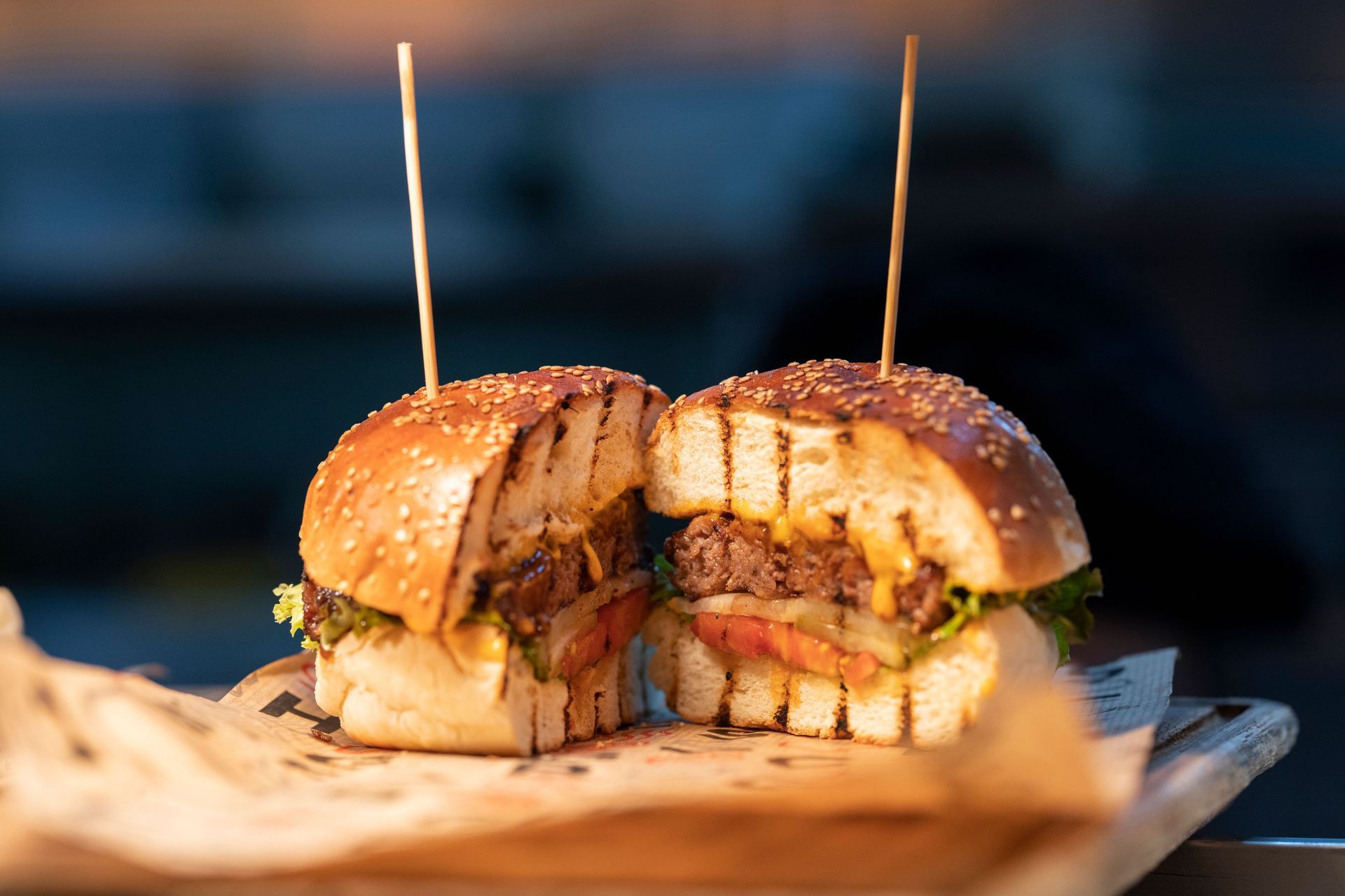Cut burger sandwich on a wooden board with two toothpicks, filled with meat, lettuce, and melted cheese