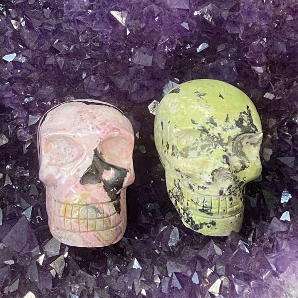 Two decorative skulls, one pink and one lime green, on a purple crystal background