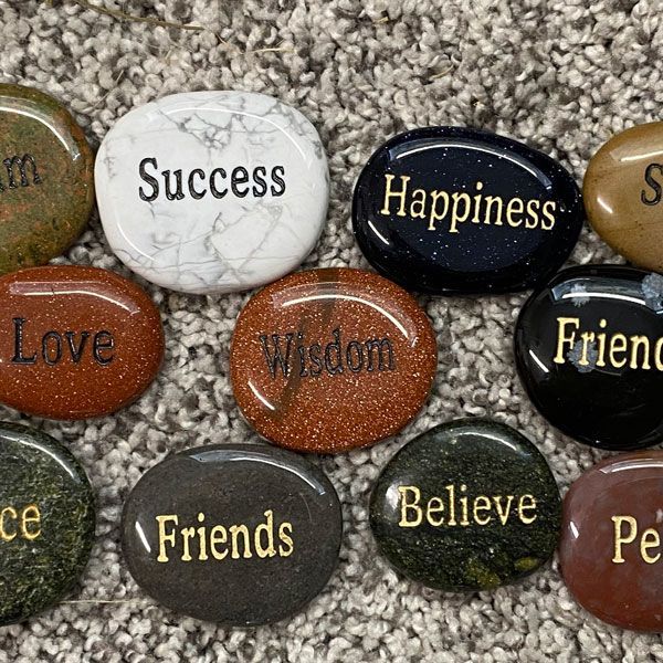 Decorative pebbles with words like “Success,” “Happiness,” “Love,” and “Friends” on a carpet.