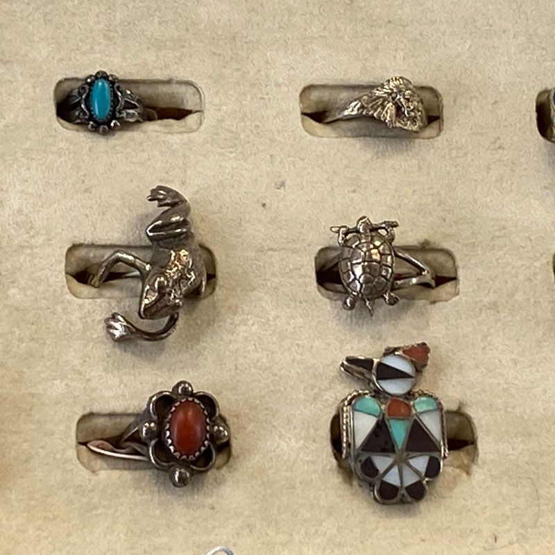 Assorted silver rings with turquoise, coral, and black geometric stones on a display board