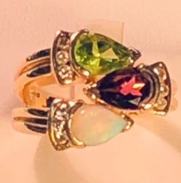 Gold ring with three teardrop gemstones: green, dark red, and opalescent white
