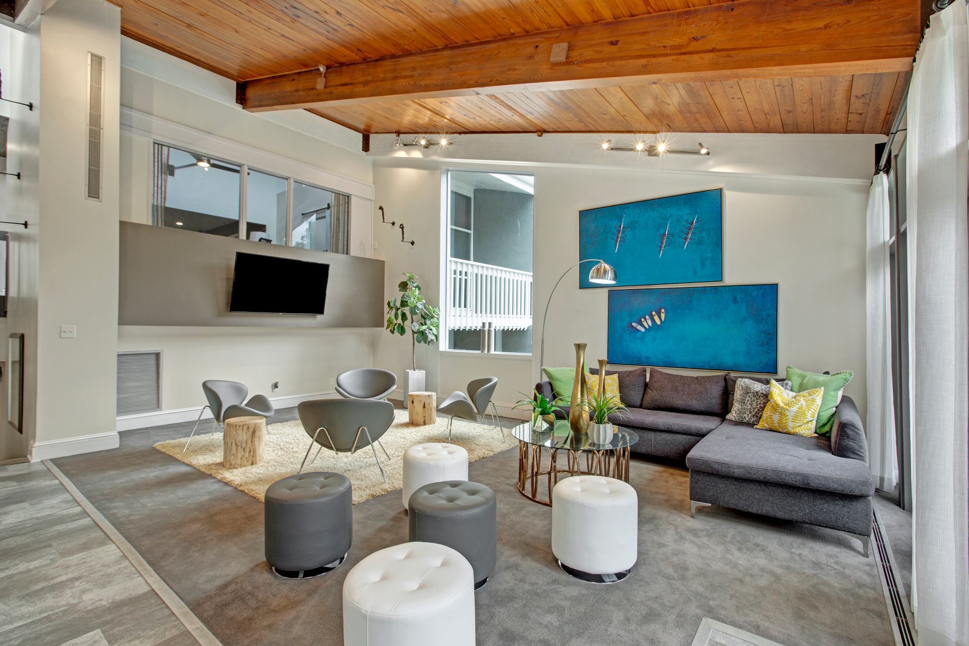 Modern living room with gray sectional, white ottomans, wall TV, and exposed wood ceiling
